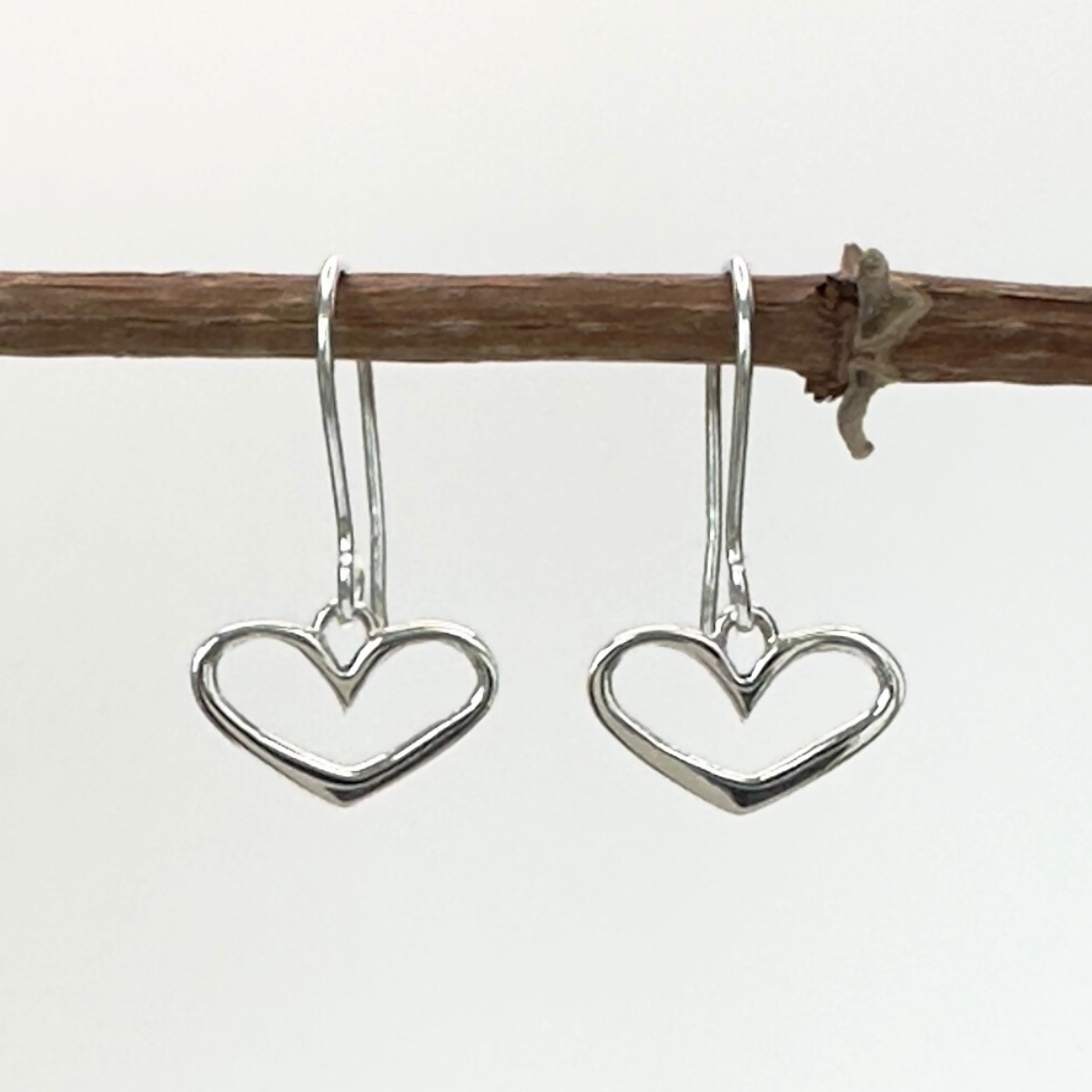 Heart-shaped silver earrings hanging from a branch on a white background