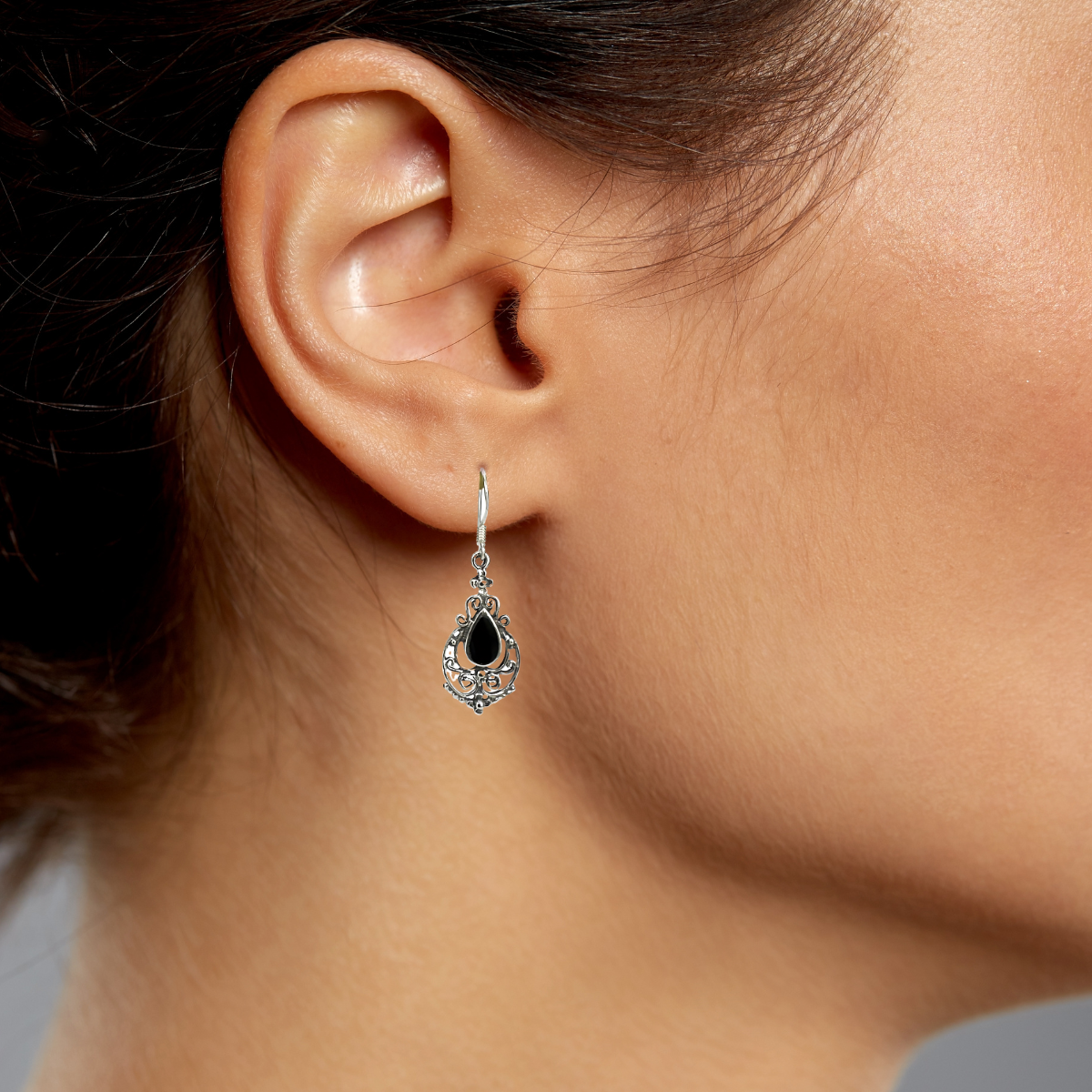 Close-up of a person wearing a black teardrop earring with a gray background