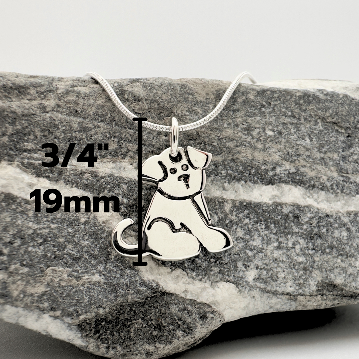 Silver dog pendant necklace on a rock with measurements displayed