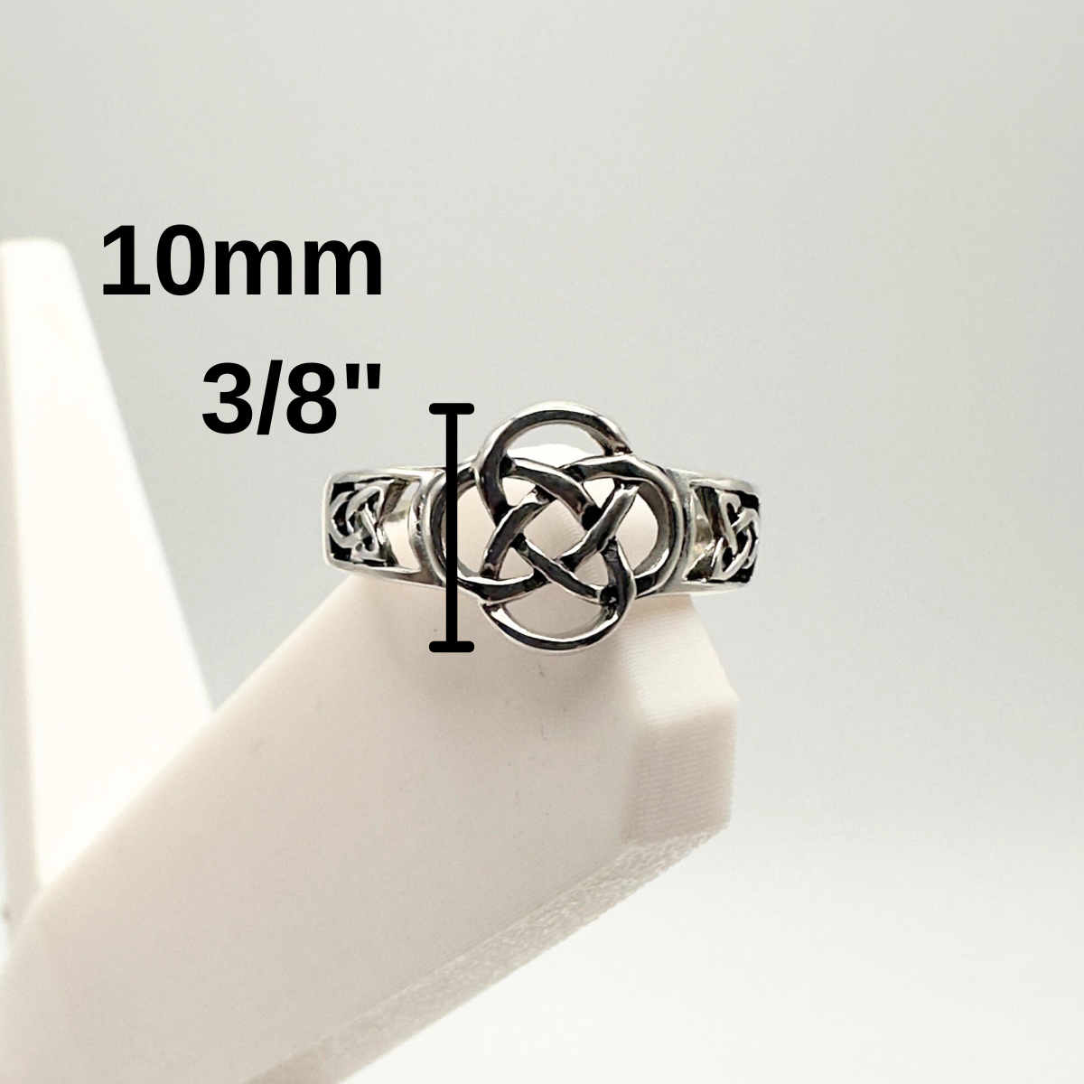 Silver ring with Celtic knot design on a white stand, showing size measurement.