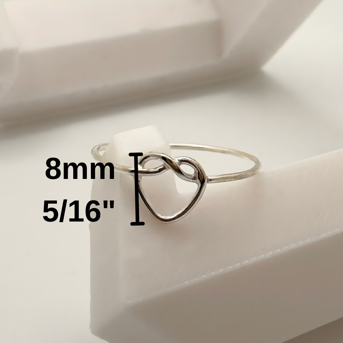 Silver ring with heart design on a white surface, showing size measurement.