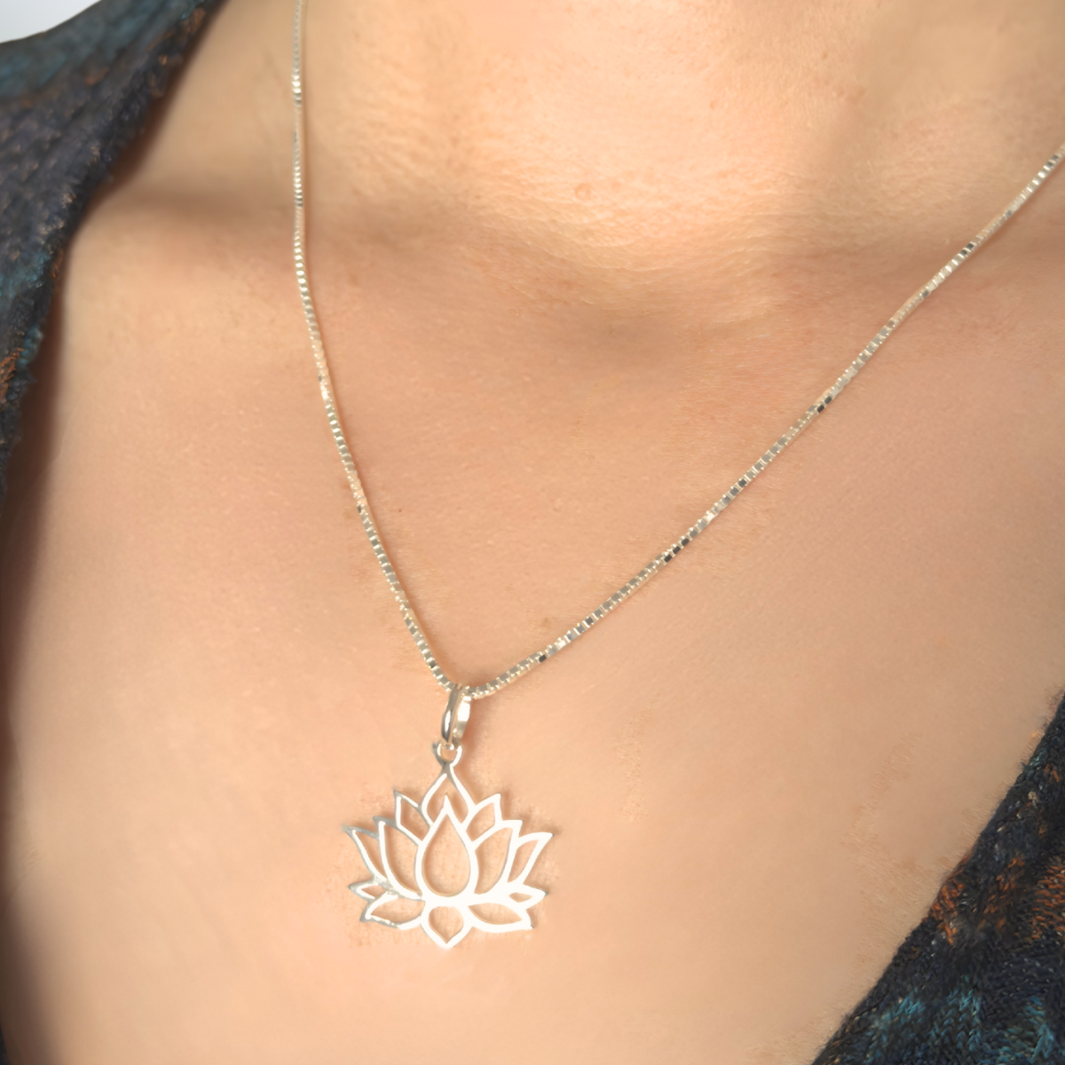 Silver lotus flower necklace on a person wearing a dark blue top.