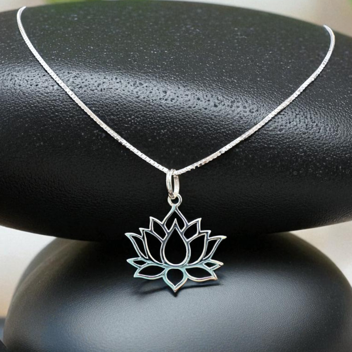 Silver lotus flower necklace on a black stone with greenery in the background