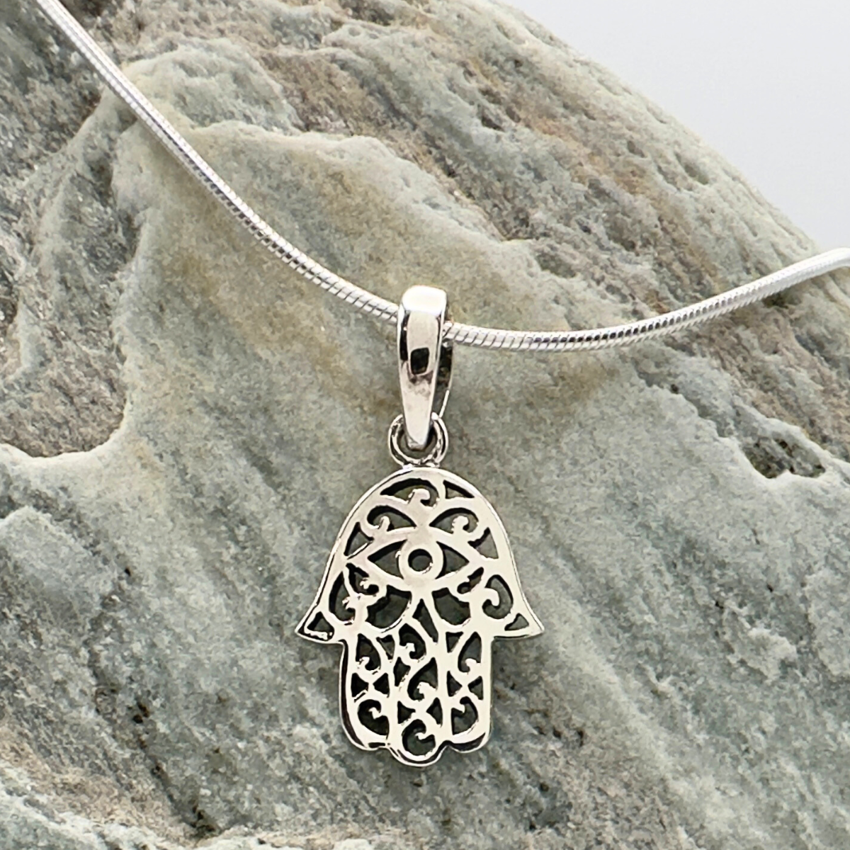 Silver Hamsa pendant on a chain against a stone background