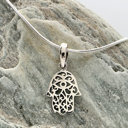 Silver Hamsa pendant on a chain against a stone background
