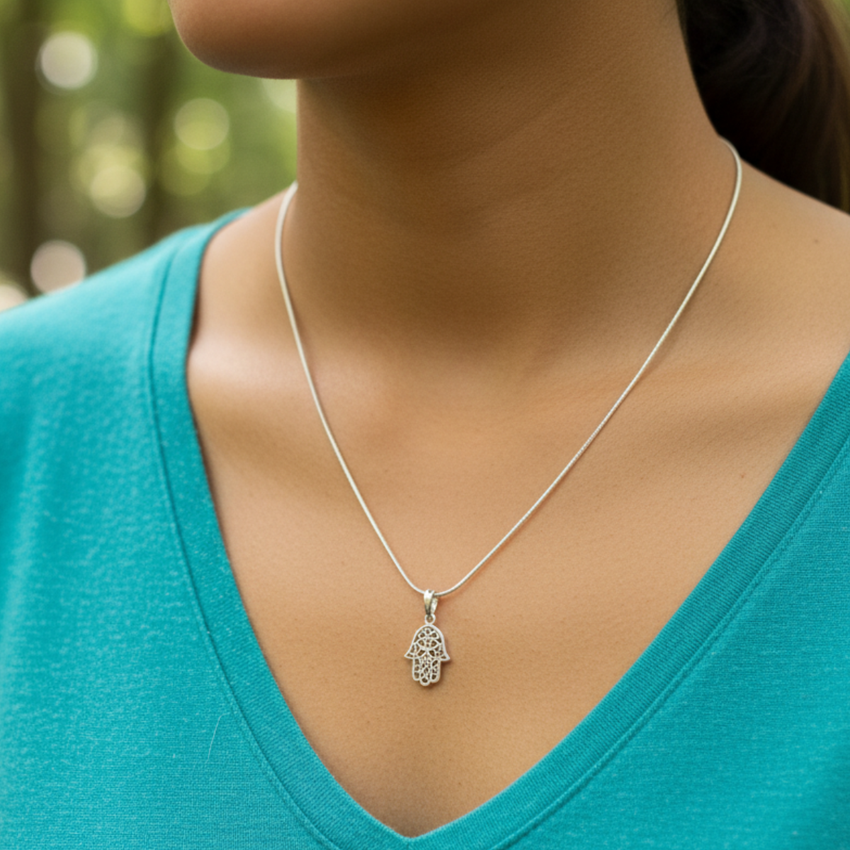 Silver necklace with a pendant worn by a person in a teal shirt against a blurred natural background