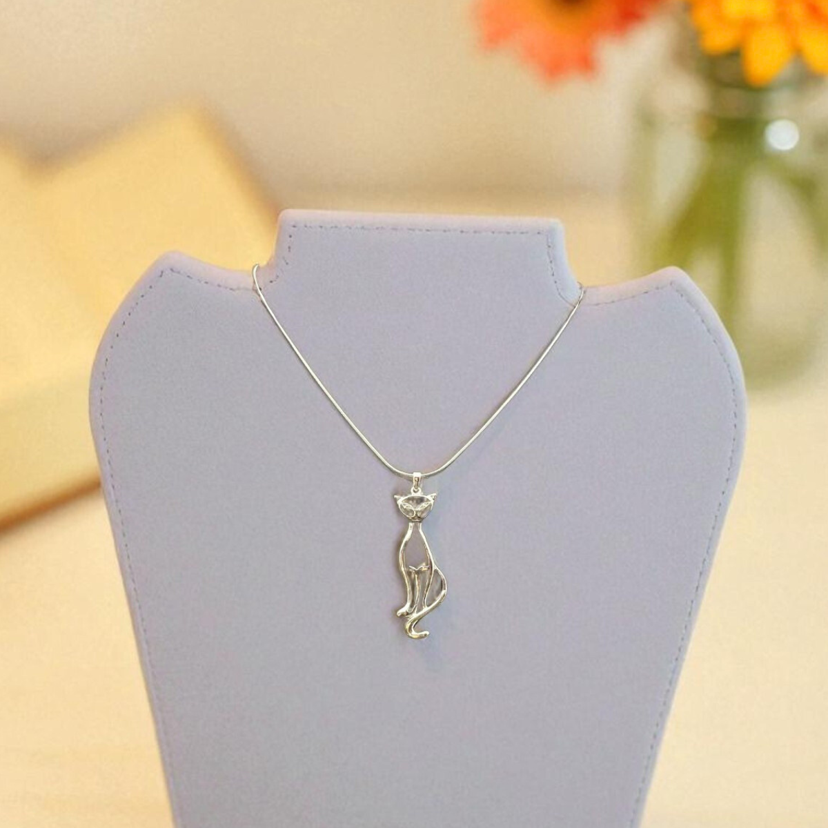 Silver necklace on a gray stand with orange flowers in the background
