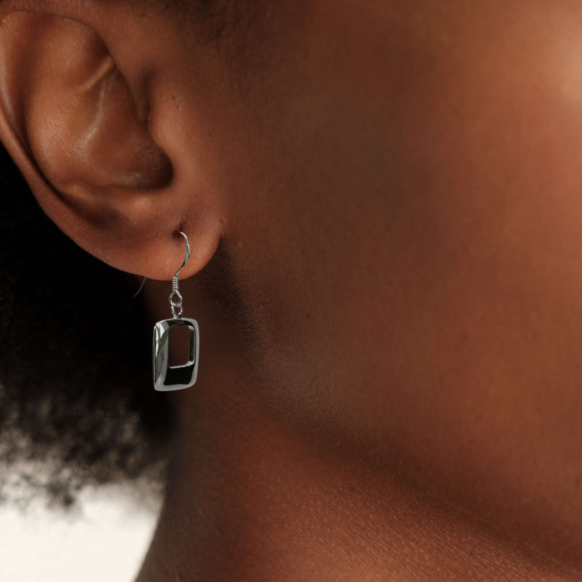 Close-up of an ear wearing a silver earring with a clear gemstone.