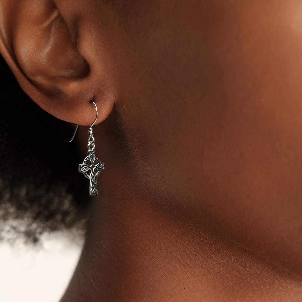 Close-up of an ear wearing a silver cross earring with a blurred background