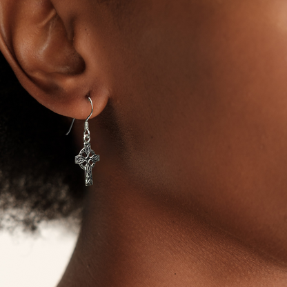 Close-up of an ear wearing a silver cross earring with a blurred background