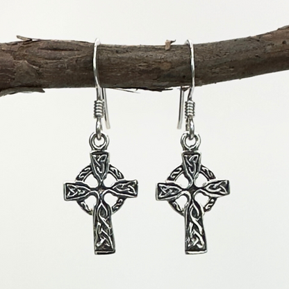 Silver Celtic cross earrings hanging on a branch with a white background