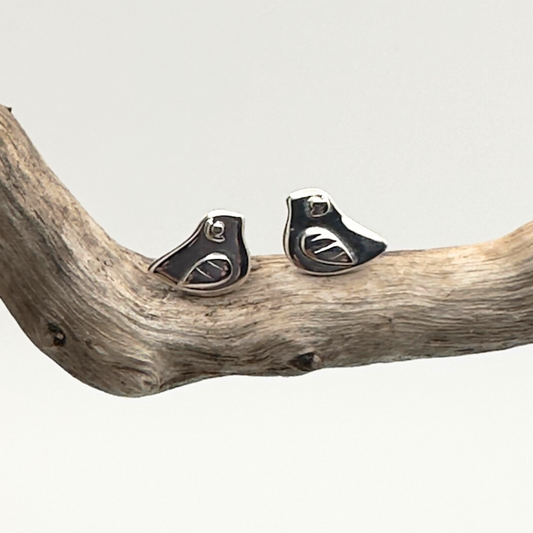 Pair of silver earrings on a piece of driftwood against a light gray background