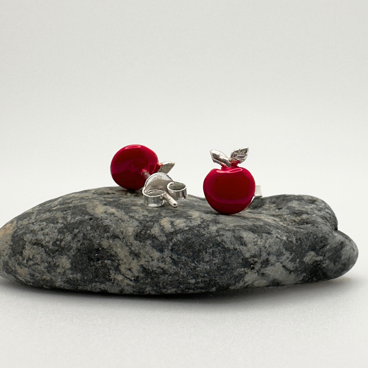 Red and silver earrings on a gray stone with a white background