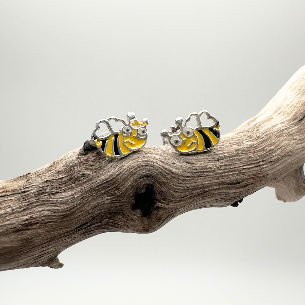 Bee-shaped earrings on a branch with a neutral background
