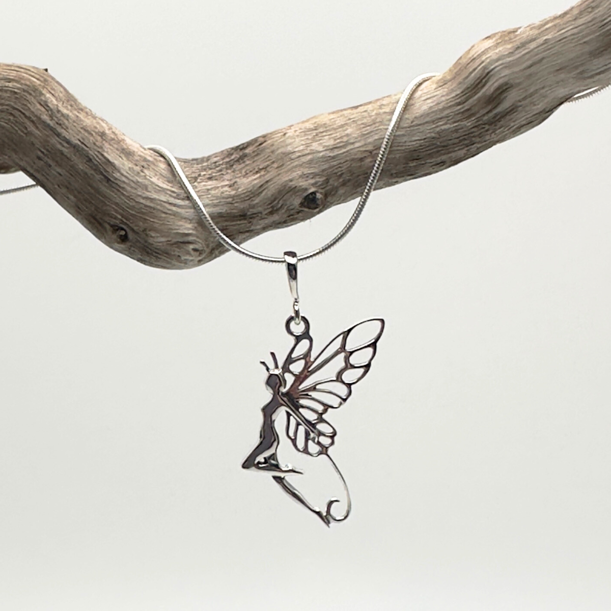 Silver fairy pendant on a chain against a light gray background