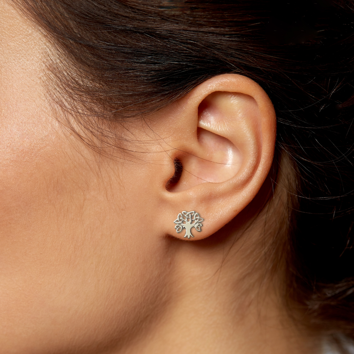 Close-up of an ear wearing a silver tree-shaped earring against a neutral background