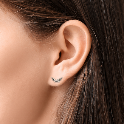 Close-up of an ear wearing a silver bat earring with blurred background