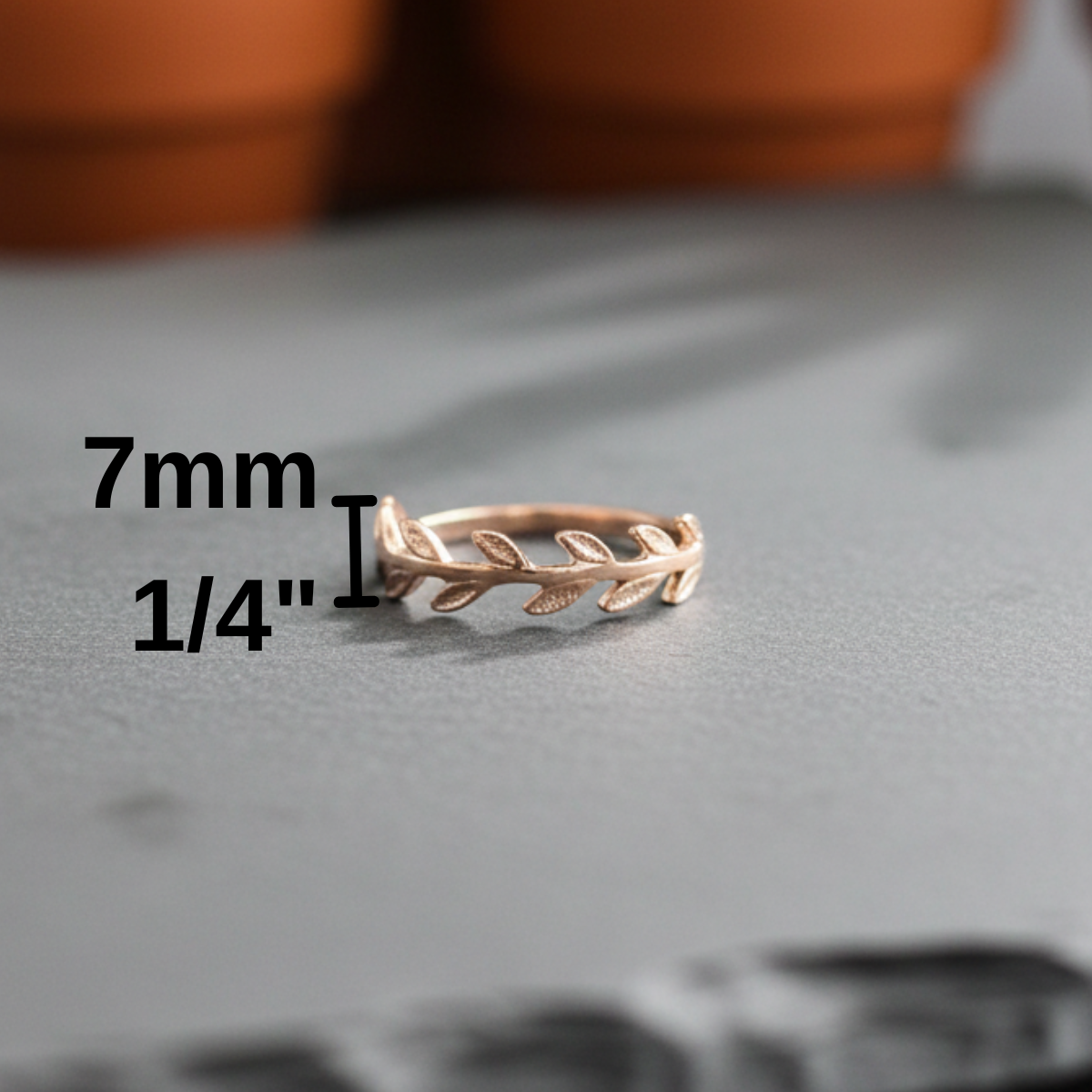 Rose gold ring with leaf design on a gray surface, measurement text overlay.