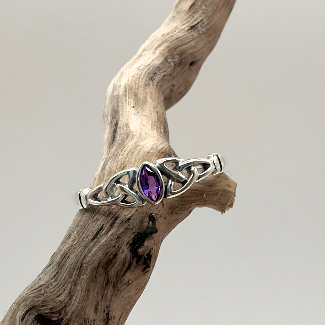 Silver ring with a purple gemstone on a piece of driftwood against a light background