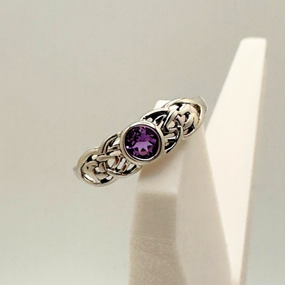 Silver ring with a purple gemstone on a white stand