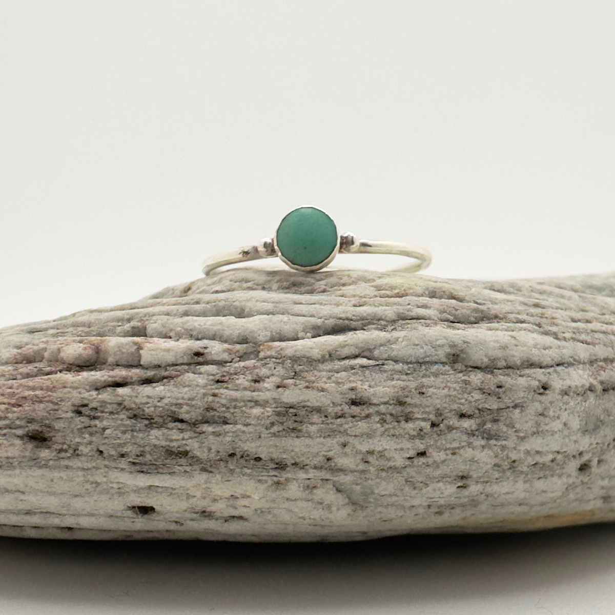 Ring with a green stone on a piece of driftwood against a white background