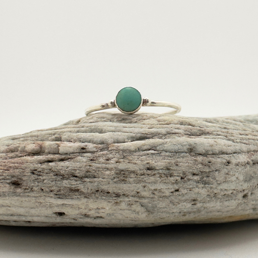 Ring with a green stone on a piece of driftwood against a white background