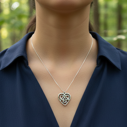 Person wearing a silver necklace with a heart-shaped pendant against a blurred forest background