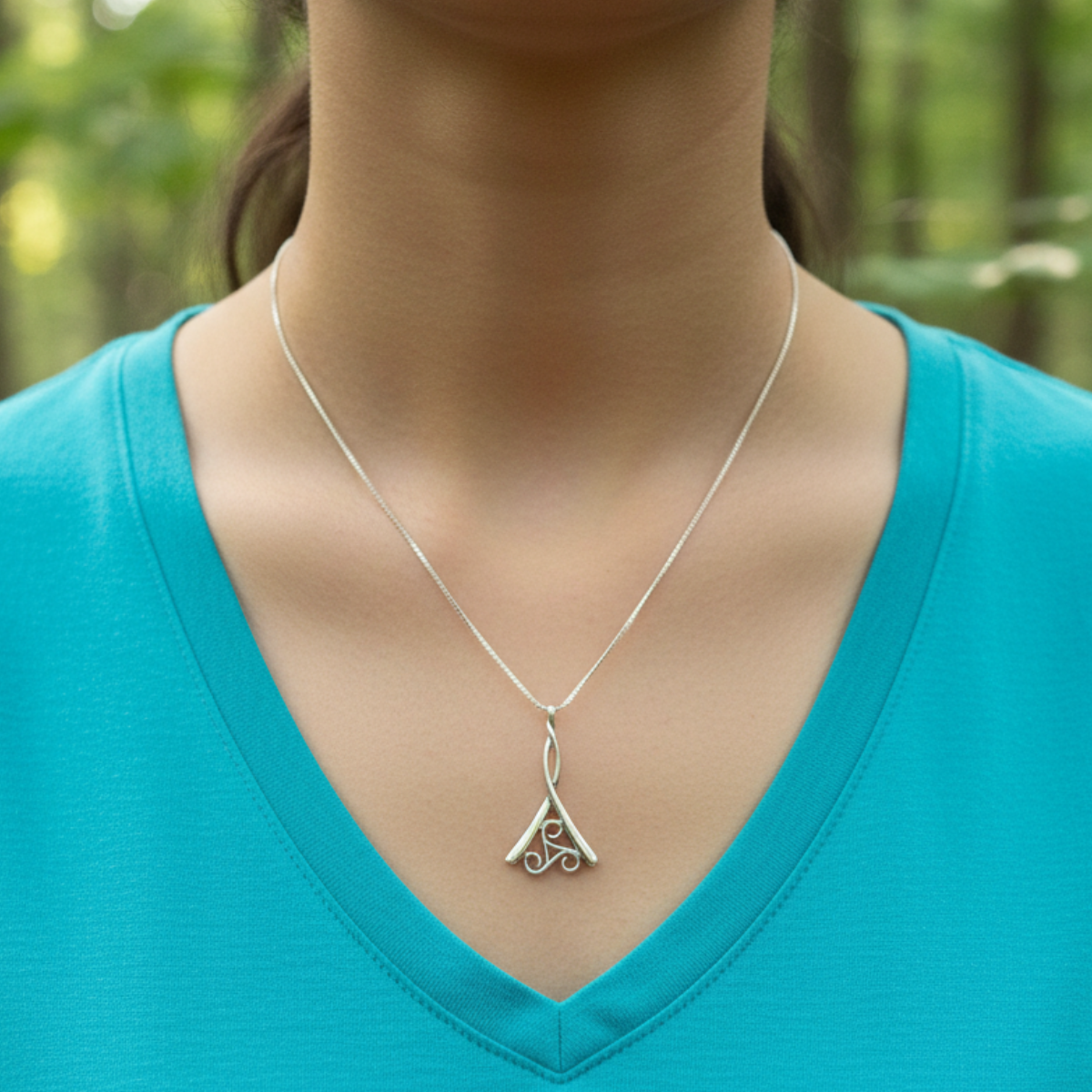 Person wearing a silver necklace with a pendant against a blurred forest background