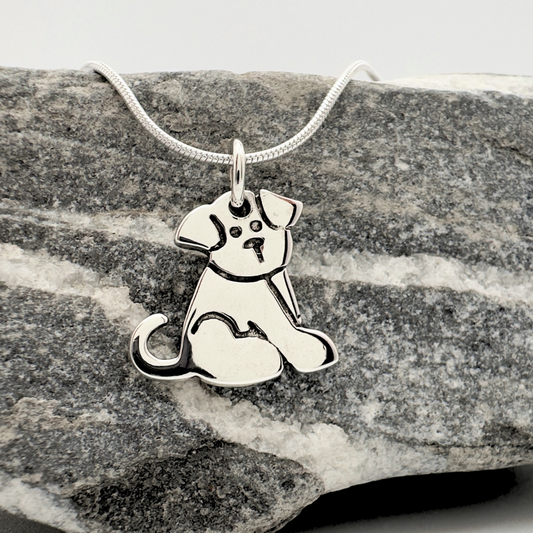 Silver dog pendant on a chain against a gray stone background