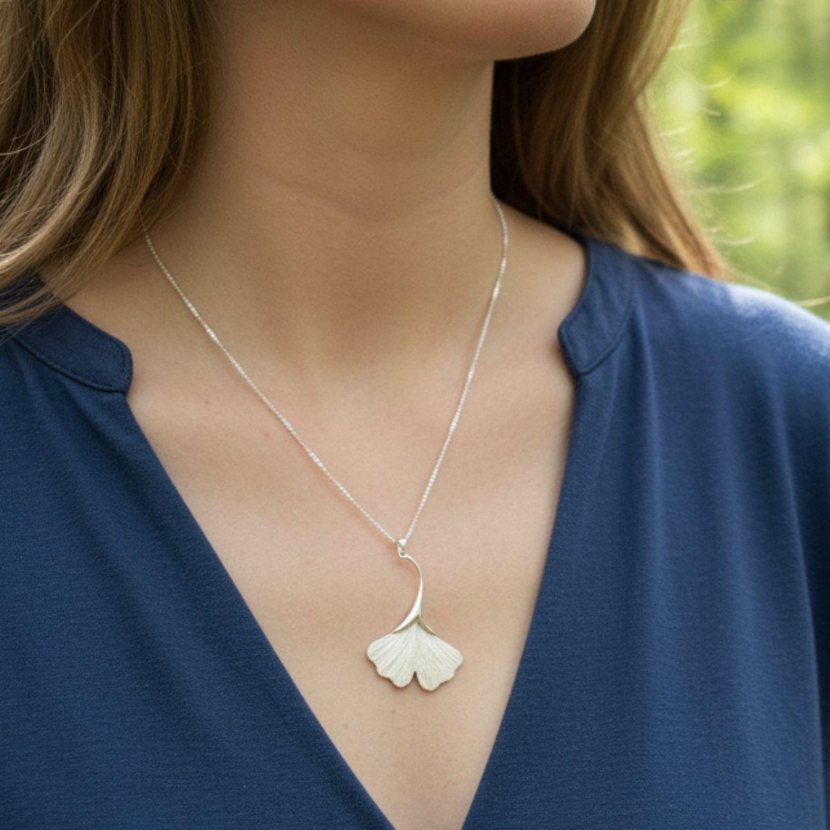 Silver necklace with a pendant worn by a person in a blue top against a blurred green background