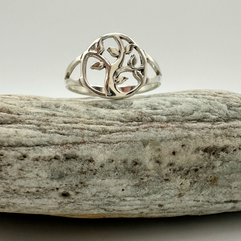 Silver ring with a tree design on a piece of driftwood against a light background
