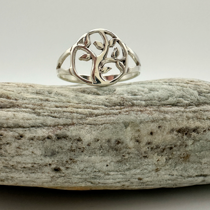 Silver ring with a tree design on a piece of driftwood against a light background