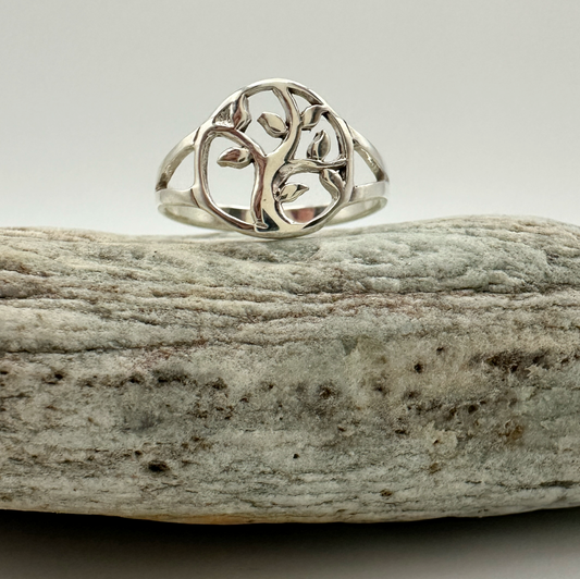 Silver ring with a tree design on a piece of driftwood against a light background