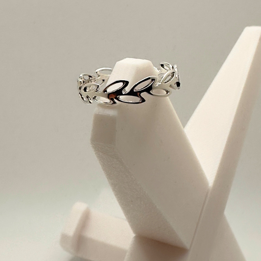 Silver ring with leaf design on a white stand against a light gray background