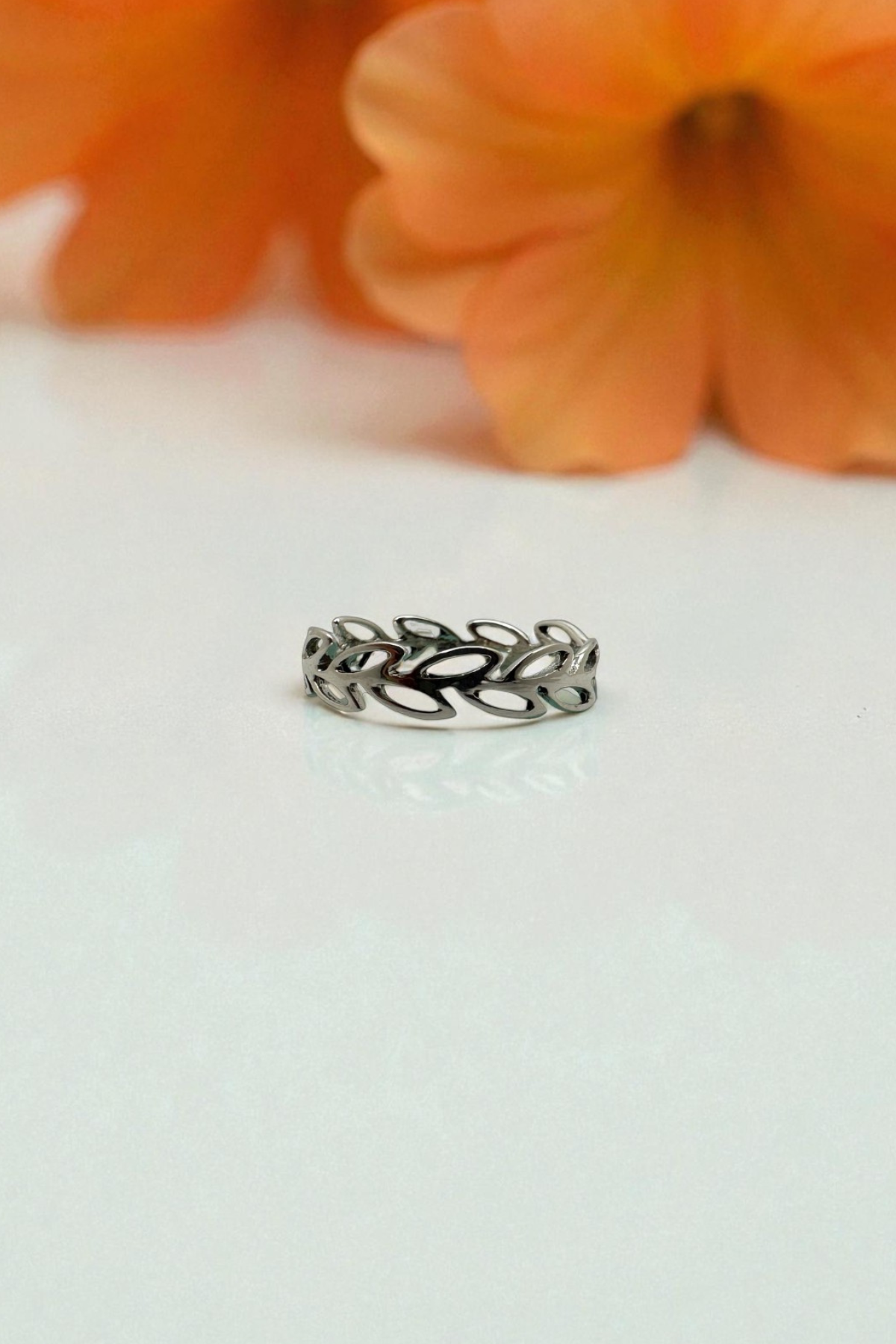 Silver ring with leaf design on a white surface with orange flowers in the background