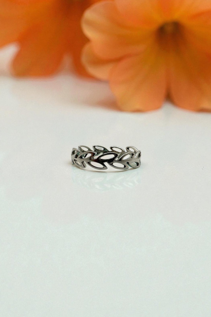 Silver ring with leaf design on a white surface with orange flowers in the background