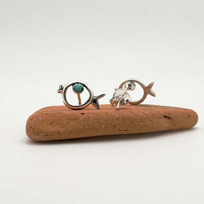 Two silver earrings with turquoise stones on a piece of driftwood against a white background