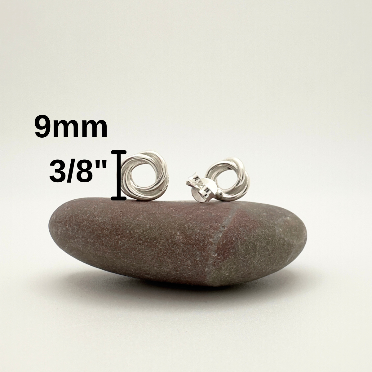 Silver earrings on a stone with measurement text on a white background