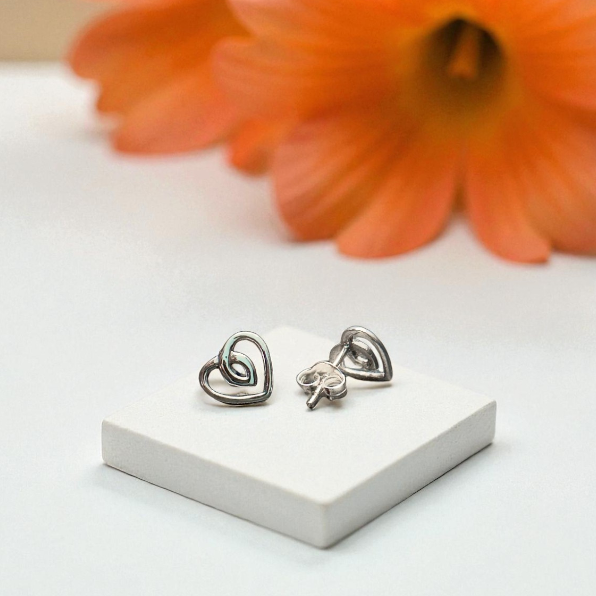 Heart-shaped earrings on a white stand with an orange flower in the background