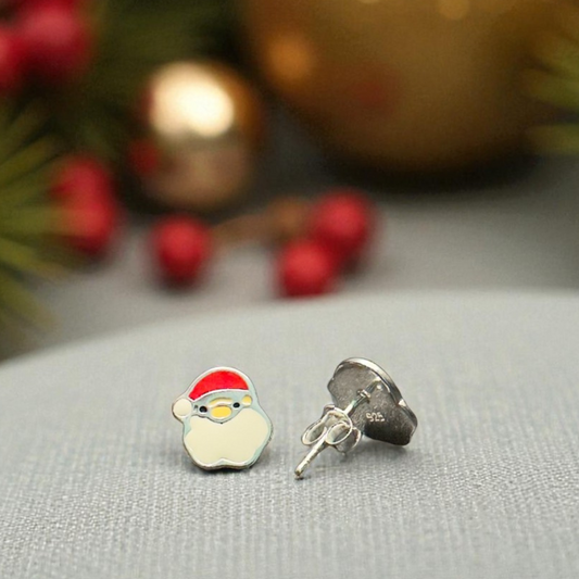 Christmas-themed earrings with a Santa Claus design on a gray surface with blurred festive background.