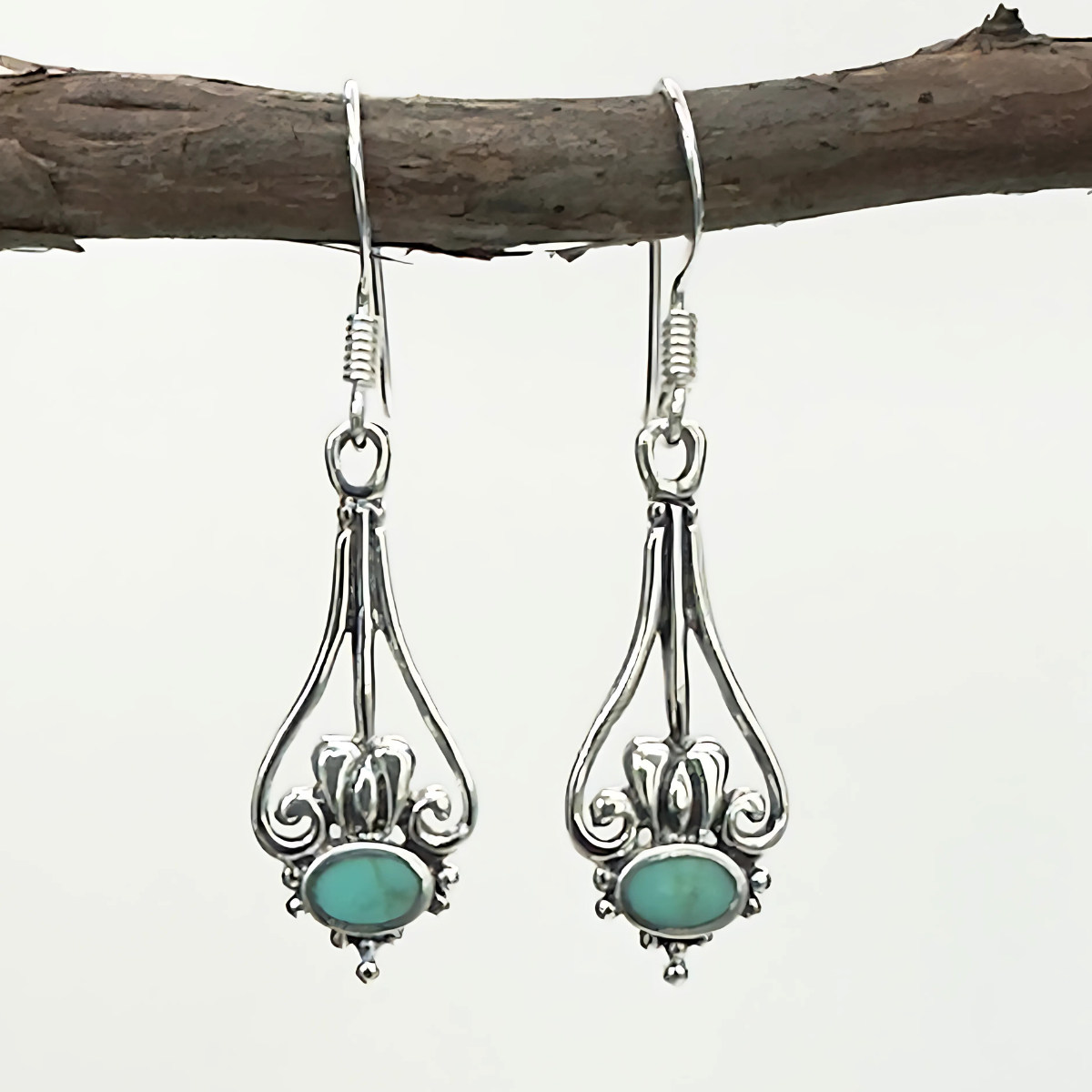 Silver earrings with turquoise stones hanging on a branch against a white background