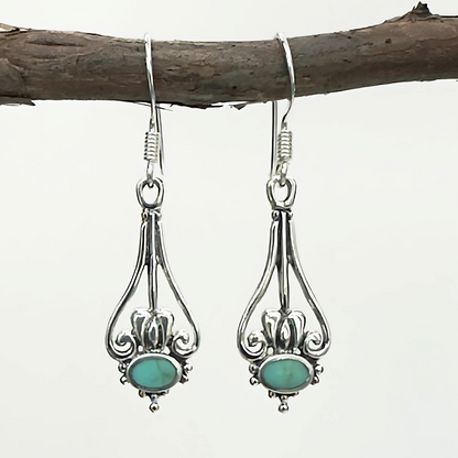 Silver earrings with turquoise stones hanging on a branch against a white background