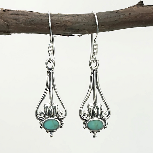 Silver earrings with turquoise stones hanging on a branch against a white background