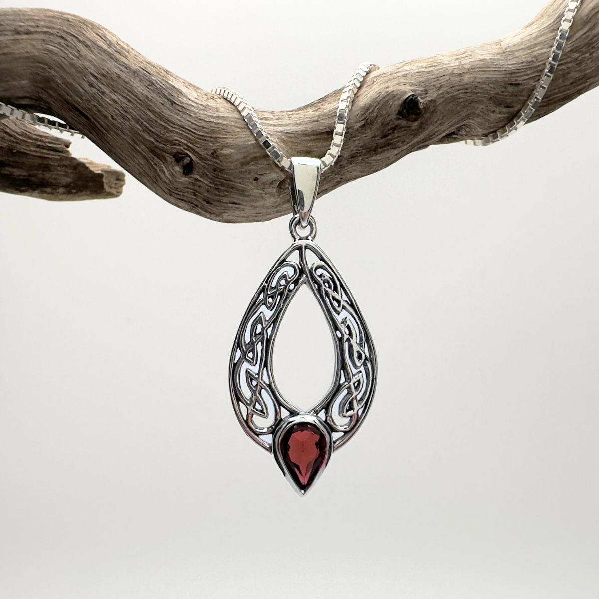 Silver pendant with a red stone on a chain, hanging from a branch against a white background