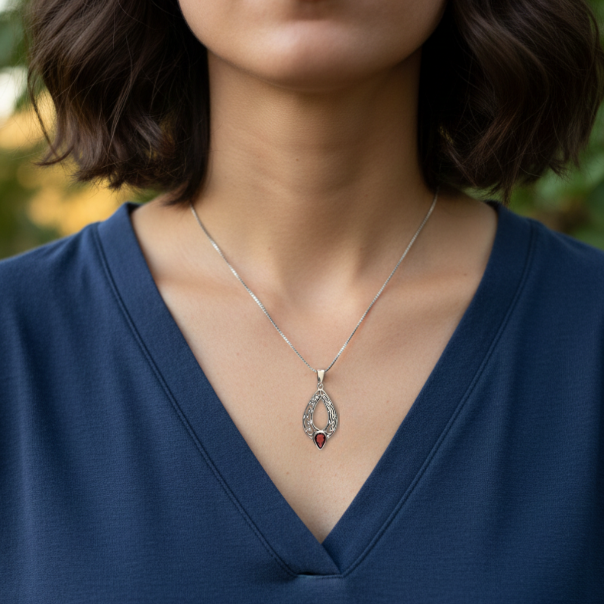 Person wearing a blue top with a necklace featuring a pendant.