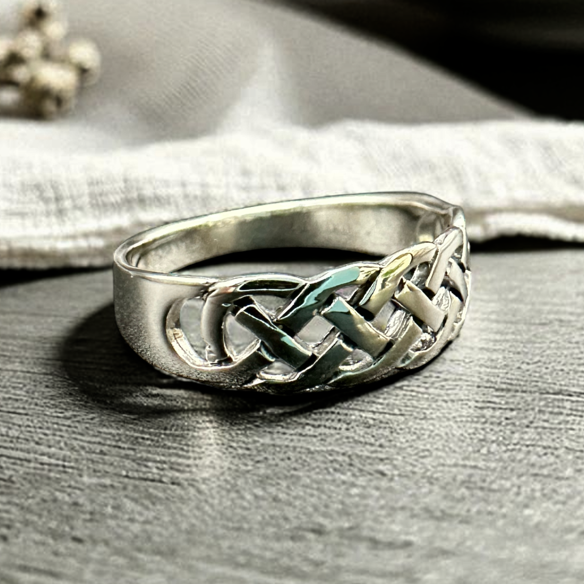 Silver ring with a braided design on a wooden surface