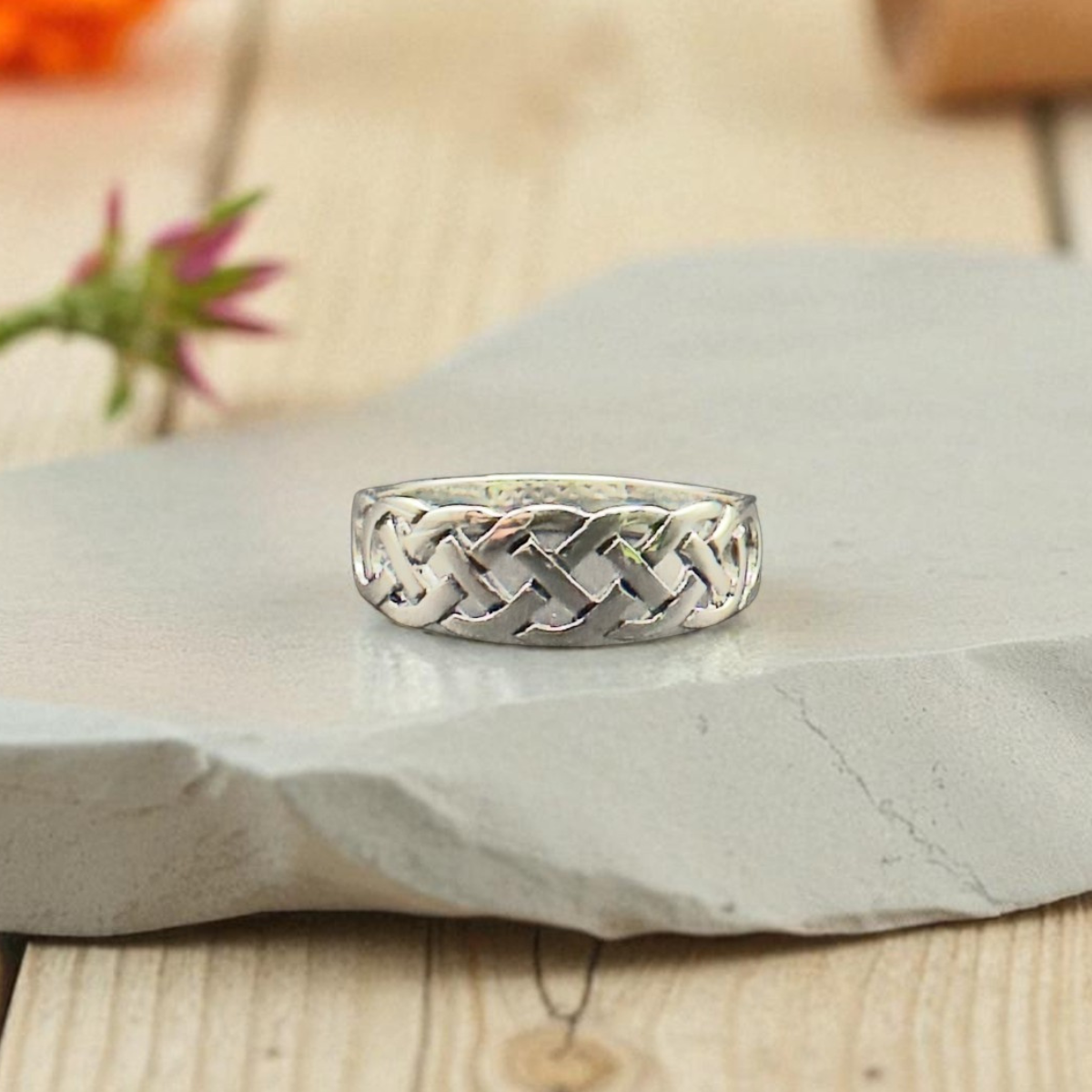 Silver braided ring on a stone surface with flowers in the background