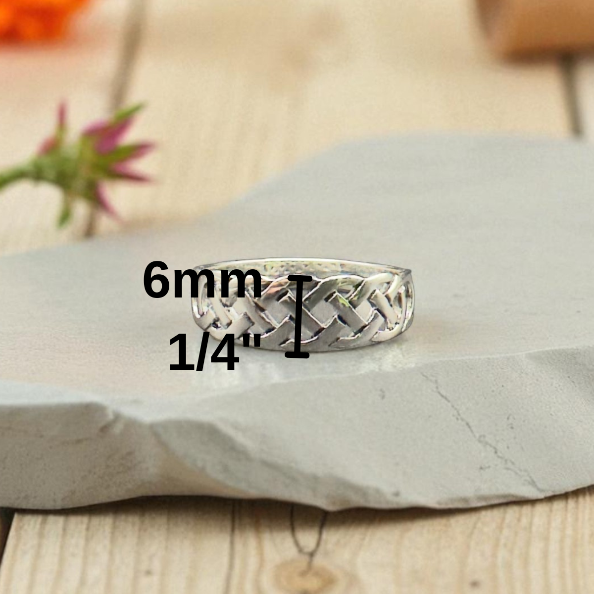 Silver woven ring on a stone surface with measurement text