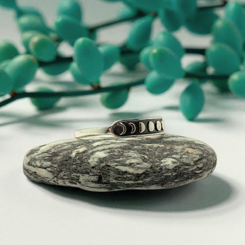 Silver ring with a stone on a white surface with green leaves in the background